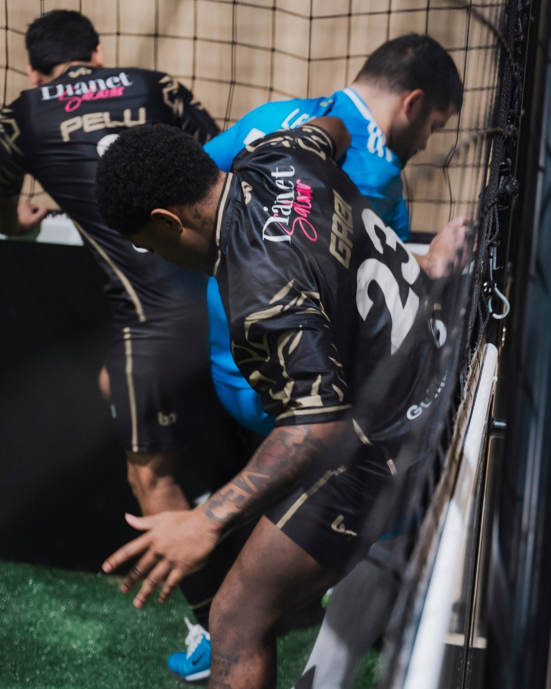 ba Gear custom soccer uniforms in action, players competing near goal on indoor field wearing black kits