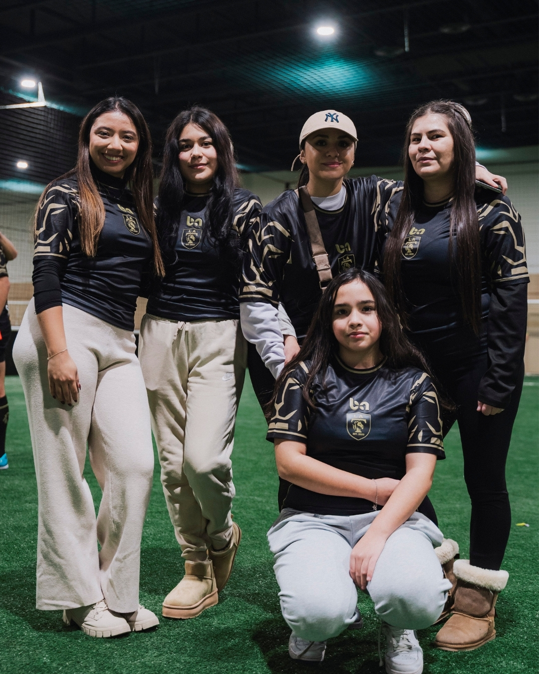 ba Gear custom team tracksuits and uniforms, women’s team posing on indoor field wearing black and gold gear
