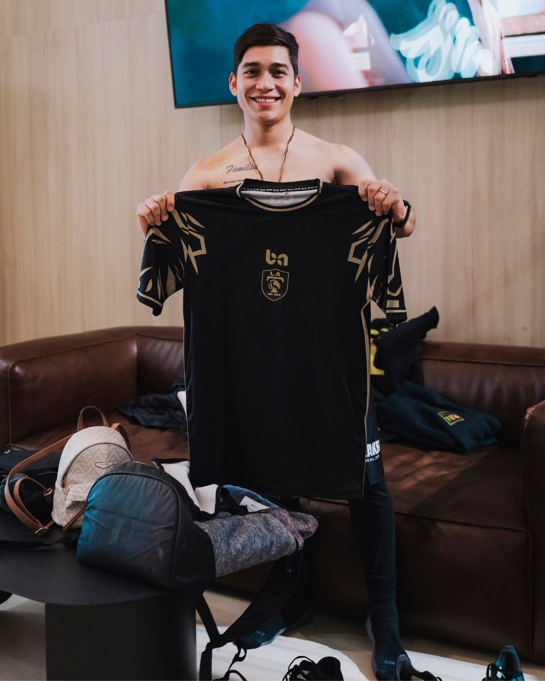 ba Gear custom soccer jersey, client holding black uniform with gold details indoors