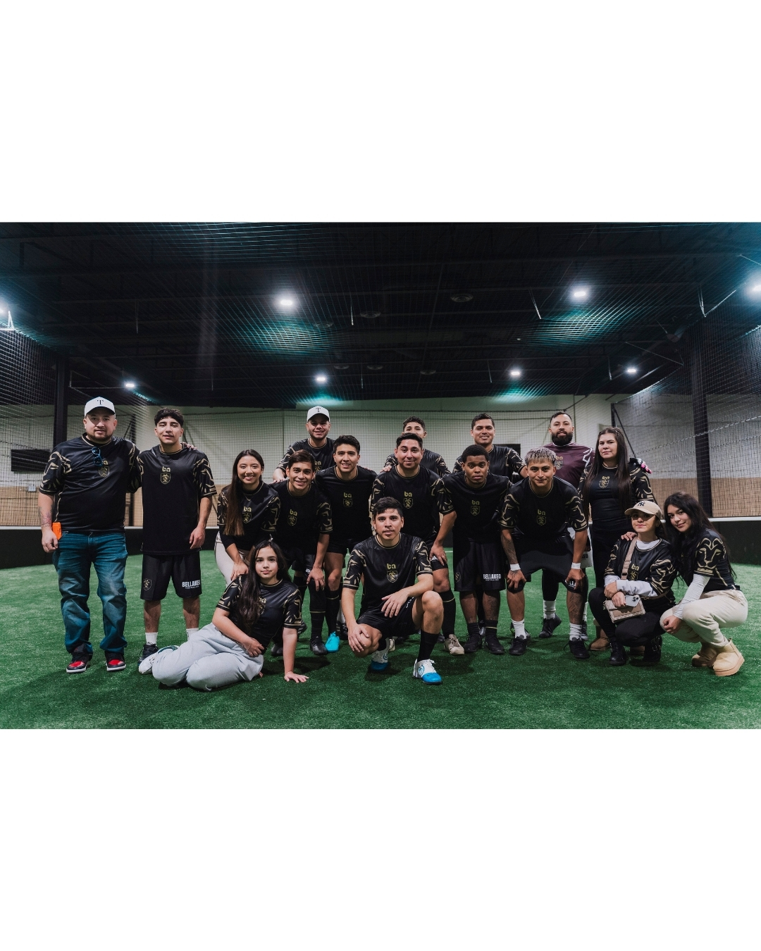 ba Gear custom soccer team group photo with players and family members wearing black uniforms on indoor field